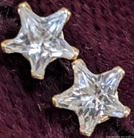 Two star-shaped cubic zirconia stud earrings set in 9K yellow gold on a dark textured surface.