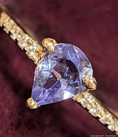 Close-up of pear-shaped light purple-blue tanzanite at the center of the gold ring with natural diamonds on the band.
