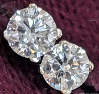 Front view close-up of two round brilliant diamonds in four-prong white gold settings on purple background