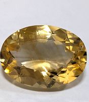 Close-up front view of oval faceted yellow citrine gemstone on white background showing the gemstone's clarity and cut.