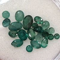 Multiple loose genuine emerald stones displayed on a white surface for clarity and color.
