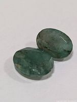 Close-up photo of two oval cut green emerald gemstones showing color and inclusions