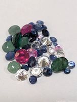 Loose mixed gemstones displayed on white background, various colors and cuts