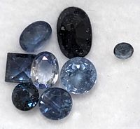 Close-up of seven genuine sapphire gemstones showcasing various cuts including oval, round, rectangular, and cabochon, in shades of blue.