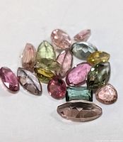 Photo showing a group of 16 assorted genuine tourmaline faceted gemstones in various colors and shapes on a white background