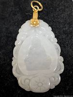 Carved jadeite pendant front view showing profile relief and surrounding floral and abstract patterns; silver bail with flower detail
