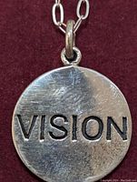 Close-up front view of necklace pendant with 'VISION' engraving