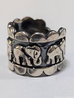 Close-up side view showing embossed elephant figures on silver ring band with scalloped edges.