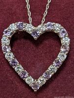 Close-up view of heart-shaped pendant featuring alternating purple alexandrite and clear stones on a red velvet background.