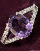 Close-up front angle of the sterling silver ring featuring an oval amethyst gemstone surrounded by cubic zirconia accents on split shank band.