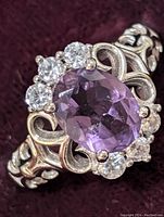 Close-up view of sterling silver ring with amethyst center stone and clear stones around it, showing ornate silver band design.