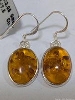 Pair of oval amber gemstone earrings set in sterling silver bezels with French hook ear wires, displayed on a white background.