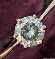 Close-up image of the sterling silver ring with round faceted moissanite gemstone held by six prongs on a smooth band.