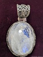 Front view of an oval moonstone pendant with blue flash set in an intricately detailed sterling silver bezel and bail.