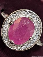Close-up of oval-shaped faceted ruby center with surrounding round cubic zirconia stones on sterling silver band