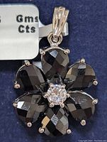 Close-up of the front of the flower pendant showing the faceted black sapphire petals and clear center stone on a dark background.