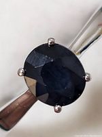 Close-up image of oval, faceted deep blue sapphire held by four prongs on polished sterling silver band.