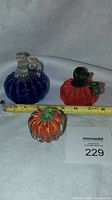 Photo showing all three blown glass pumpkins - one blue, one larger orange, and one smaller orange item beside a measuring tape for scale.