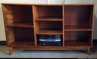 Front view of mid century modern open front wood cabinet with multiple adjustable shelves and tapered legs.