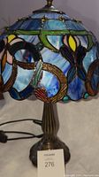 Full lamp showing blue stained glass shade with floral and geometric designs and bronze base