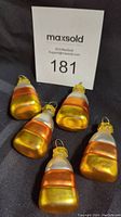 Five blown glass candy corn shaped ornaments arranged on black fabric.