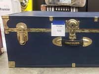 Front view of blue wooden steamer trunk showing two brass latches, central lock and black handle with 'Concourse' branding.