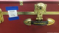 Close-up of brass latch, lock, and handle marked 'CONCOURSE' showing wear and brass edges.
