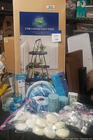 Boxed unopened Wilson & Fisher 3-tier A-frame plant stand with long dimensions. In front are blue glass votive holders, blue pillar candles, and many white votive candles and tealight candles in plastic packaging.