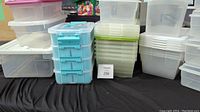 Multiple stacks of assorted plastic storage containers in clear and semi-transparent plastic with various lid colors, including a blue 4-tier latch container.