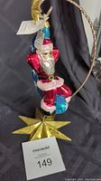 Front view of Santa ornament hanging from metal ring with golden star base, includes tag.