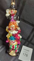 Front view of Radko glass clown totem ornament showing three stacked clowns in colorful costumes and smiling faces, black background.