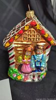 Front view of ornament showing Hansel and Gretel in front of gingerbread house with candy and floral details.