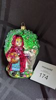 Front view of Radko Little Red Riding Hood glass ornament with wolf and tree foliage background, showing detailed hand-painted features and gold hanging loop.