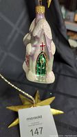 Front view of Radko glass church Christmas ornament showing snowy roof, green door, and red cross window detail.