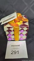 Front angle showing purple and white diamond pattern on gift box with orange-yellow bow and attached tag
