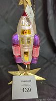 Front view of Christopher Radko rocket ornament with pink and purple details and gold glitter highlights.