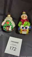 Photo showing both Radko glass ornaments: Wee Berrie House and Sledding Kid, side by side on a black background with MaxSold tag