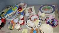 Overview of the lot showing plates, bowls, cups, a toy rattle, a photo frame and other child dining and toy items