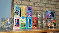 Wide view of 16 Disney-themed collector cups and glasses including boxed and unboxed items with colorful character art.