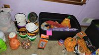 Photo shows ceramic pumpkin and ghost-shaped containers, a green Frankenstein container, artificial leaves in a plastic bag, and black plastic totes containing more decorations like a purple witch sign and other pumpkin decor.