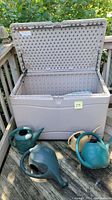 Opened Lifetime plastic storage bin showing interior and three plastic watering cans outside.