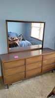 Front full view of the mid-century wood dresser with attached large rectangular mirror reflecting window and room