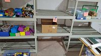 Gray plastic shelving unit shown with various boxes and containers for scale. Shelves have ribbed surface and appear sturdy.