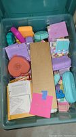 Overview of bin containing multiple pastel-colored Polly Pocket compacts and instruction booklet