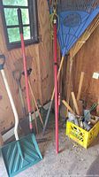 Photo of yard tools including various rakes, shovels, and garden tools stored in a shed with wooden walls.