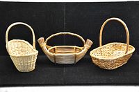 Photo of three assorted wicker baskets with handles on a black background showing different shapes and weaving patterns.