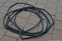 Photo of a coiled black rubber garden hose on a stone tile floor, showing metal fittings on both ends.