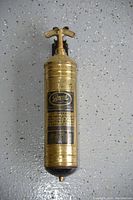 Full view of the brass antique fire extinguisher showing T-handle, brass body, and label.