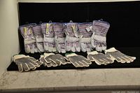 12 pairs of assorted work gloves displayed on black backdrop, including 7 pairs of striped leather gloves and 5 pairs of gray mesh gloves with black rubber dots.