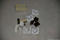 Photo showing 11 electrical accessories: 4 square timers, 1 round timer, 1 rectangular timer, 5 plug extensions/adapters in white, beige, and dark colors on a gray floor.